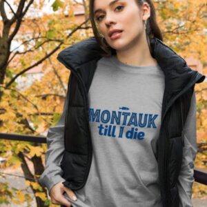 Woman wearing a stylish Montauk sweatshirt, standing near the beach on a breezy day.