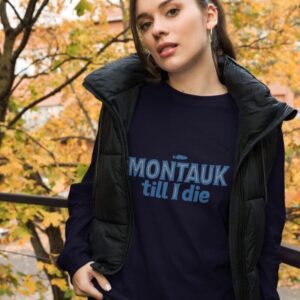 Woman wearing a stylish Montauk sweatshirt, standing near trees on a breezy day.