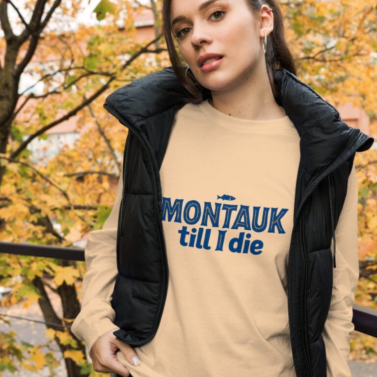 Woman wearing a stylish Montauk sweatshirt, standing near the beach on a breezy day.