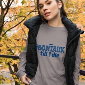 Woman wearing a stylish Montauk sweatshirt, standing near the beach on a breezy day.