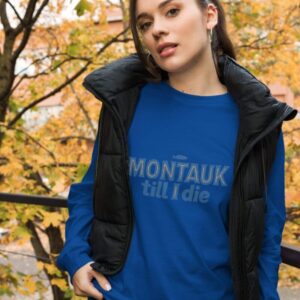 Woman wearing a stylish Montauk sweatshirt, standing near trees on a breezy day.