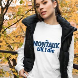 Woman wearing a stylish Montauk sweatshirt, standing near the beach on a breezy day.